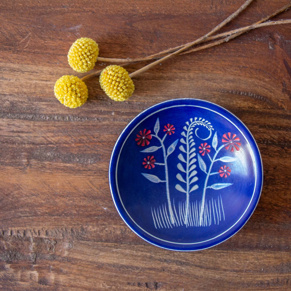 
                  
                    Blue ceramic plate with floral design on a wooden surface with yellow flowers and branches.
                  
                