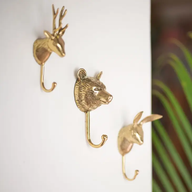 A collection of solid brass coat hooks, including deer, bear, and rabbit, hanging on a wall