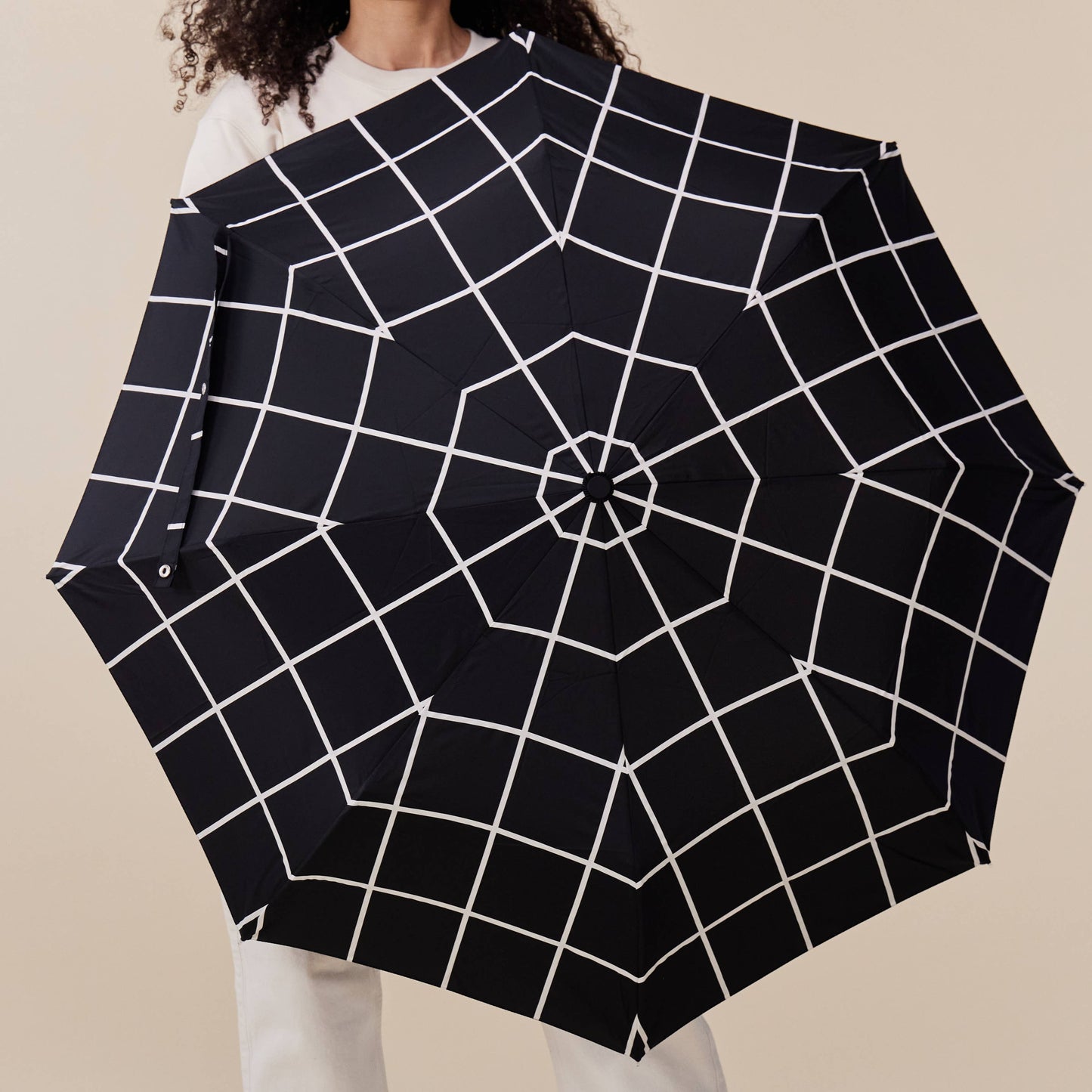 
                  
                    A woman carrying an opened duckhead umbrella in black grid pattern.
                  
                