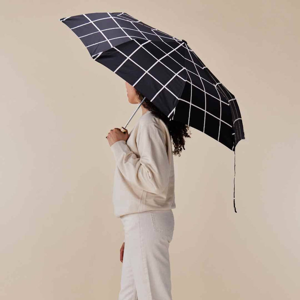 
                  
                    Woman carrying the original duckhead umbrella, opened, with a black grid pattern
                  
                