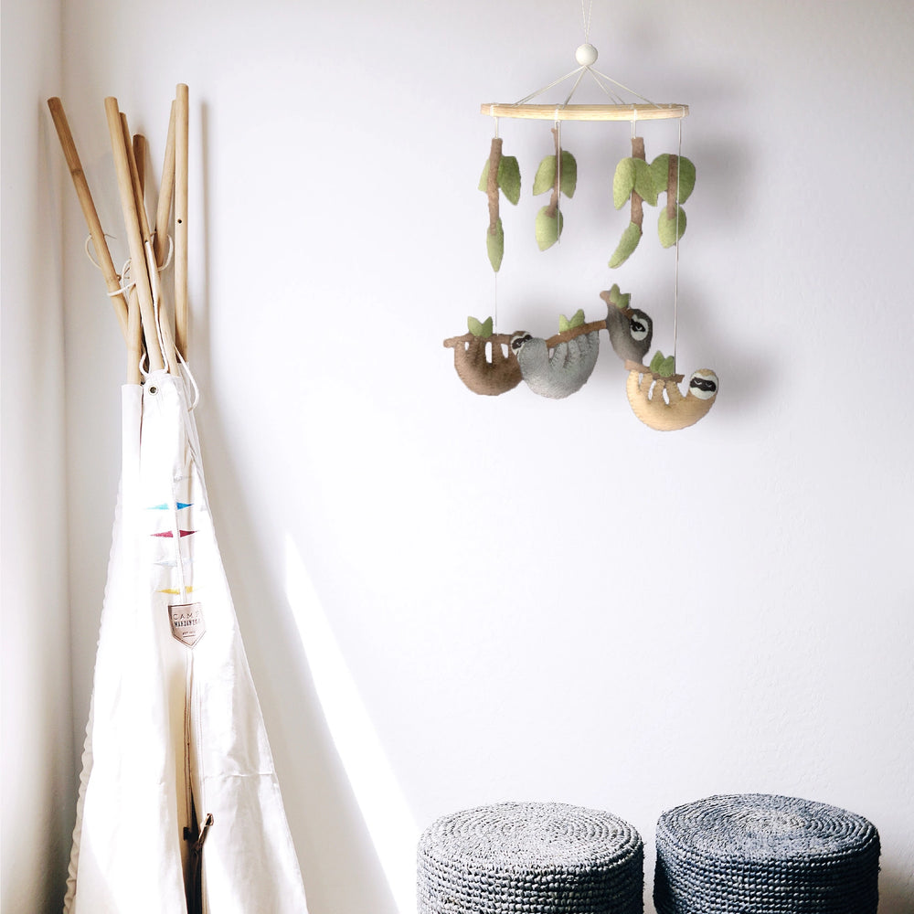 Felt crib mobile with four hanging sloths and hanging leaves around a natural wood frame