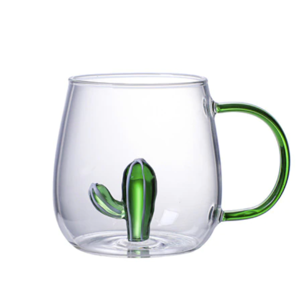 A clear glass mug with a green handle and hand fused glass cactus at the bottom