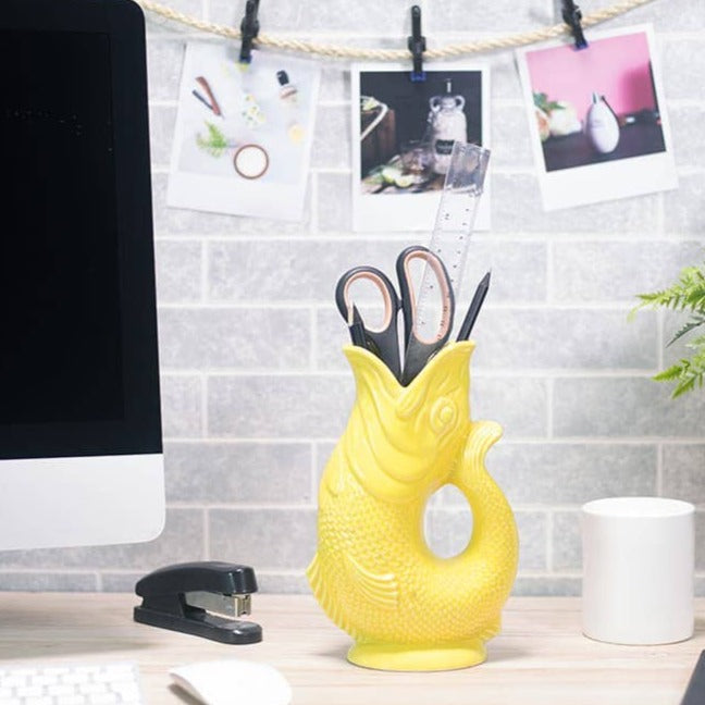 The gluggle jug original gurglepot in yellow holding office supplies