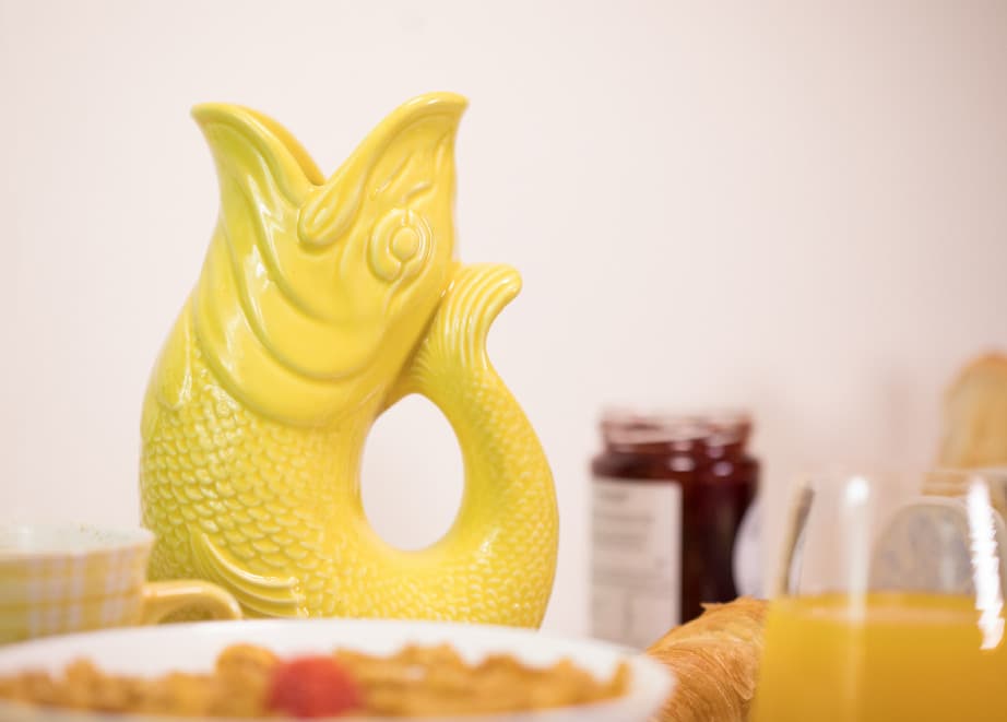 
                  
                    The original gluggle jug gurglepot fish pitcher in yellow on a kitchen table at meal time
                  
                