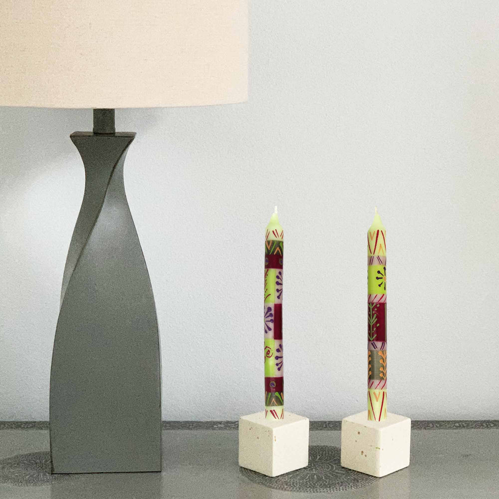 
                  
                    Two decorative candles on white stands next to a gray lamp with a beige shade.
                  
                