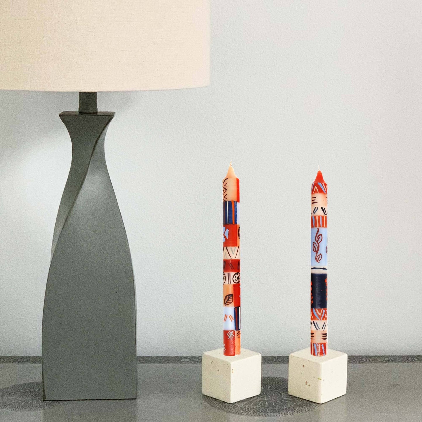 
                  
                    Two decorative candles on white stands with a lamp in the background
                  
                