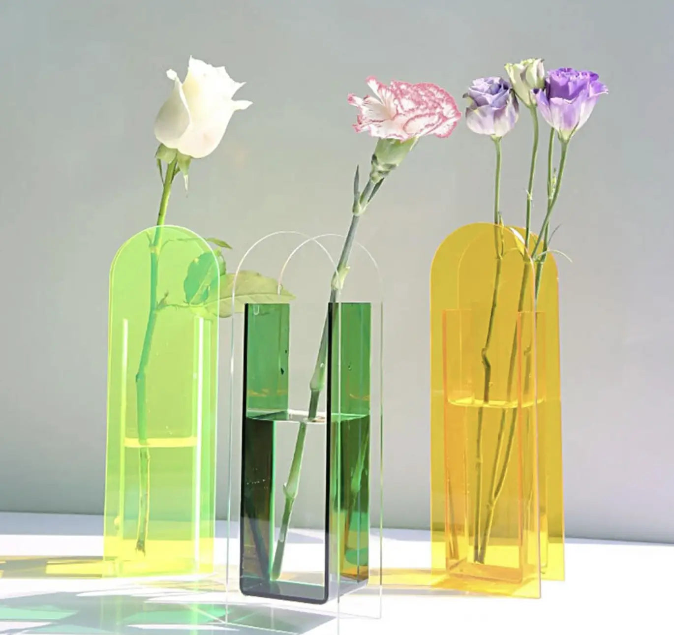 Transparent acrylic flower vases in bright yellow, green, and yellow holding water and carnations