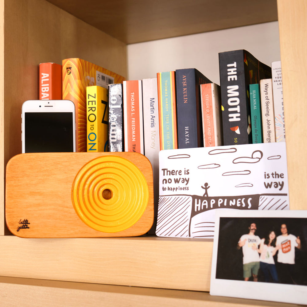 
                  
                    Wooden sound system in yellow on a book shelf loaded with an iPhone.
                  
                